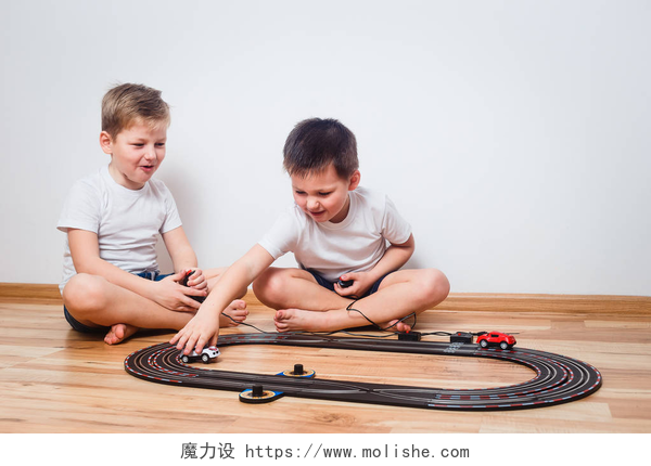 白色墙壁前的两个小孩坐在地板上玩跑车穿着白色 t恤衫的学龄前儿童在室内赛道上租车